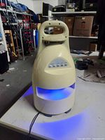 Front view of beige Brookstone outdoor speaker with carry handle and blue LED lit band