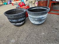 Two large black plastic planter pots side by side outdoors