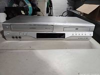 Front view of Toshiba silver DVD/VCR combo showing display, DVD tray, VHS slot and front AV jacks