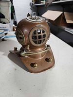 Front and side view of miniature diving helmet showing copper body, brass grills and fittings