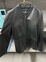 Front view of black leather jacket on hanger showing overall design and brand tag