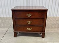 Front view showing three drawers, brass pulls, walnut finish, decorative base