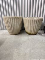 Pair of matching fluted planters on concrete floor showing texture and moss