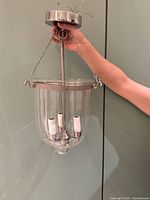 Full view of pendant light held by hand showing canopy, chains, stem, glass shade, and three sockets