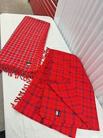 Two red tartan flatweave throws folded on table with fringe visible