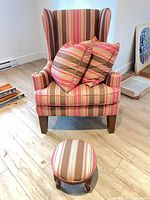 Front view of striped wingback chair with two pillows and matching footstool