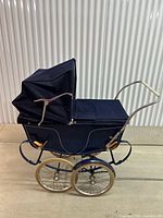 Side view of navy coach pram showing hood, apron, chrome handle and wheels