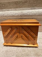 Closed wooden accordion box front view showing metal-linked arms and wood tone