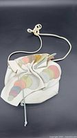Full view of white leather drawstring bag with multicolored appliqués and shoulder strap