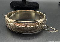 Side view of hinged sterling silver gold-filled bangle showing floral engraving and safety chain