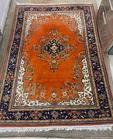 Full view of orange Persian rug showing central medallion, border and fringe