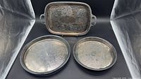 Overall view of three silver-plated trays: one rectangular with handles, two round gallery trays