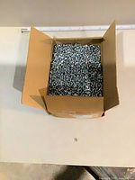 Open cardboard box filled with small machine screws