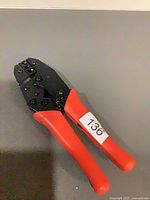 Full view of crimping pliers with red handles on grey surface