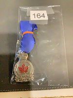 Medal in clear plastic sleeve with blue ribbon folded, inventory sticker visible