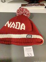 Full view of red knit beanie showing CANADA lettering and pom-pom