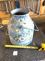 Front view of distressed blue floral metal milk can with tape measure for scale