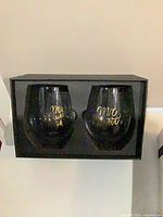 Box containing two smoked glass stemless wine glasses with gold script lettering