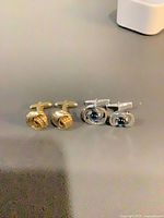 Gold-tone knot cufflinks next to silver-tone cabochon cufflinks