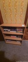 Full view of light oak 3-shelf bookcase with VHS tapes on two shelves