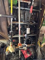 Several string trimmers in front of shelving with stacked wheels and spare engine heads