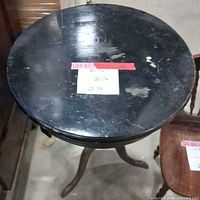 Full view of black round pedestal side table showing overall design and wear