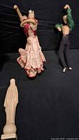 Two cloth dancer dolls and Madonna statue on black backdrop