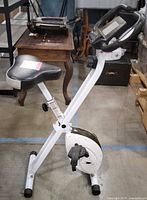 Side view of white foldable exercise bike showing frame, seat, and drive unit
