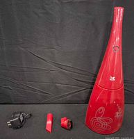 Full view of red handheld vacuum standing upright with charger and two attachments