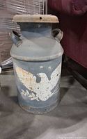 Front view of metal milk can showing eagle graphic and rust patina