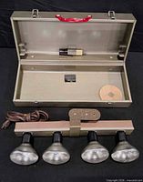 Open metal case showing lamp bar with bulbs, cord, spool, adapter