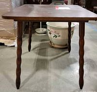 Front view of square wooden table showing carved legs and scratches on top