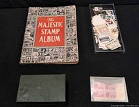 Lot overview showing album, plastic tray of loose stamps, green tin, packet of stamp blocks