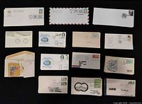 Group of 14 stamped and postmarked envelopes laid out on black background showing stamps, cachets and cancellations