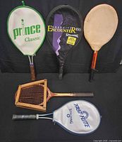 Five rackets laid out, four in covers and wooden racket in press