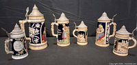 Front view of six German beer steins showing relief decoration and pewter lids