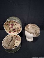 Styrofoam head with wig, open green wig case showing second wig and floral interior