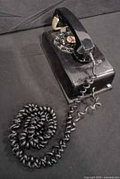 Full view of black rotary wall telephone with handset and coiled cord