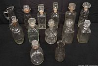 Group shot of all twelve clear glass decanters and bottles on black backdrop
