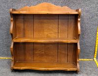 Front view of wooden wall shelf showing two shelves and scalloped top