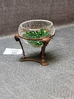 Brass ram head stand holding crackle glass bowl filled with green stones, overall view