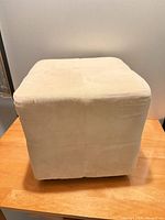 Front-side view of beige cube ottoman showing upholstery and shape