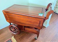 Side view of wooden bar cart with drop leaves closed, showing large spoked wheel and lower bottle rack cutouts