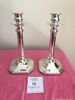 Front view of both silver-plated St. James candlesticks on pink surface