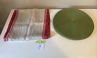 Folded beige table runner with red borders next to one round green placemat