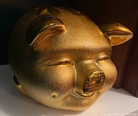 Front view of gold ceramic piggy bank showing face and coin slot