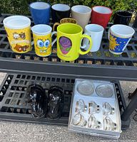 Overview of ten assorted mugs on top shelf, black bookends and boxed tea set on lower shelf