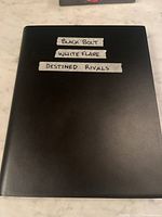 Closed black binder with masking-tape labels naming included sets.