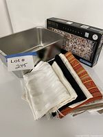 Group shot of stainless steel pan, puzzle box, stack of table runners