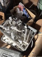 tote with numerous PVC fittings, coil of white tubing and surrounding boxes